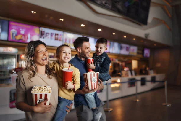 familia joven y feliz con palomitas de maiz y bebidas en el cine